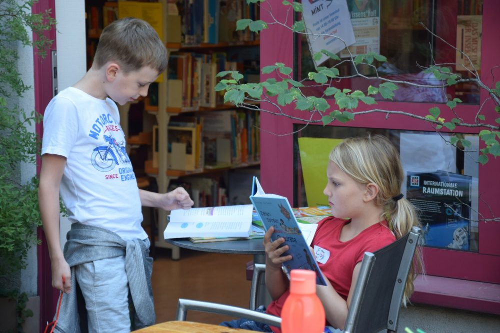 Zwei lesende Kinder im Hof der Bücherei