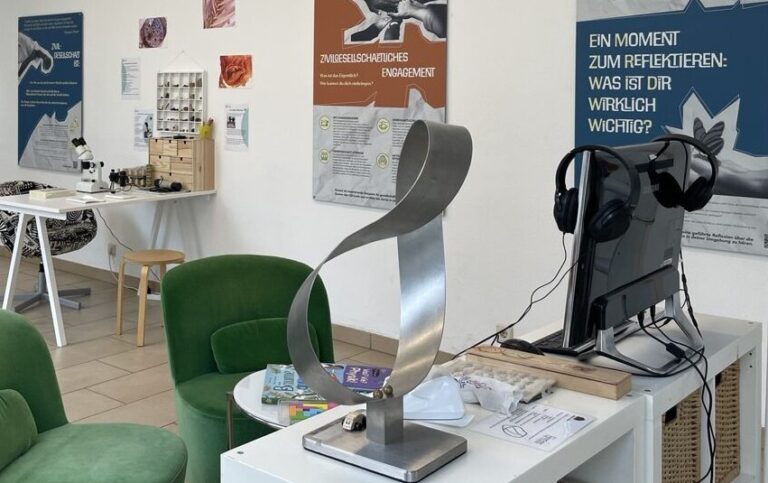 Das Bild zeigt den Innenraum des Wissensraumes. Im Vordergrund sind zwei grüne Sessel zu sehen, im Hintergrund sieht man die Ausstellungsplakate an der Wand.